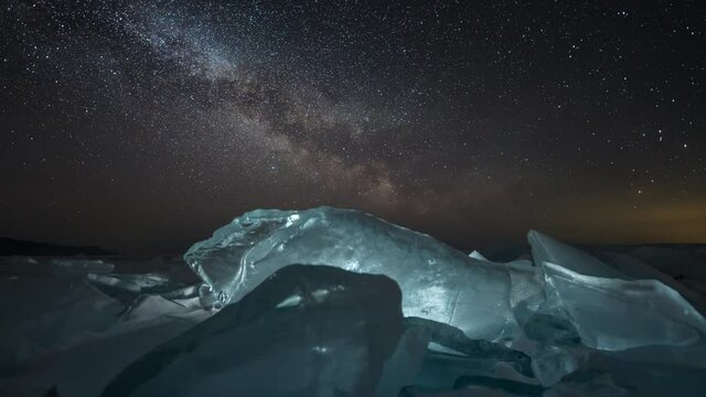 Time lapse of milky way. Rotating stars at night. Big blue lit ice blocks. Baikal lake in winter time.