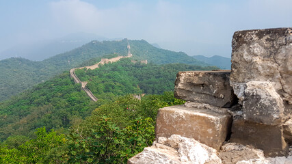 Fototapeta na wymiar A panoramic view on a renewed Jinshanling part of Great Wall of China. The wall is spreading on tops of mountains. Many watchtowers on the peaks. Dense forest around it. World wonder. Tradition