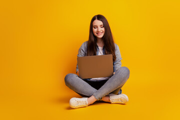 Naklejka premium Portrait of girl with laptop sit floor crossed legs on yellow background