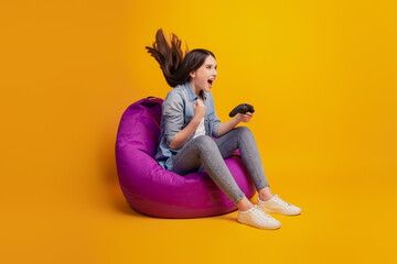 Portrait of girl keep the joystick in hand while playing video games sit beanbag on yellow wall © Tetiana
