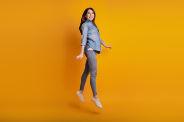 Fototapeta na wymiar Portrait of active cheerful energetic girl jumping isolated on yellow background
