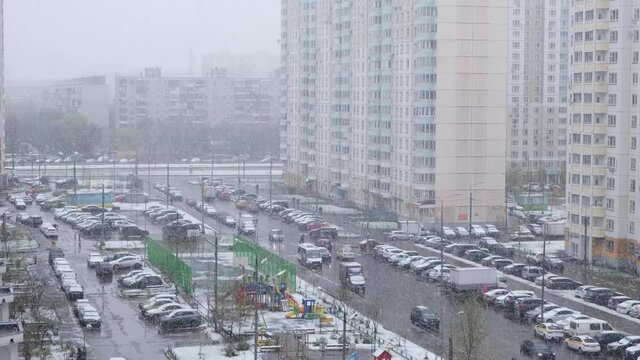 Snowfall in the city in spring (April). Top view from the window to multistorey buildings, street, playground and courtyard.