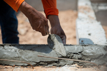 Closeup hands of the workers were plastering cement concrete on the walls with trowel at house construction site.