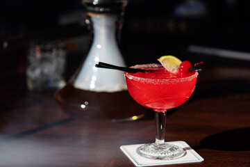 Raspberry alcoholic cocktail in a glass with foam sprinkled with freeze-dried raspberries in the hookah smoke on the table.