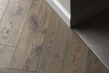Room corner, three different textures: grey wall, natural oak wood floor, stone dark grey tiles