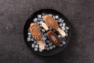 Chocolate popsicles and crushed ice on black stone. Top view
