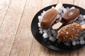 Chocolate popsicles and crushed ice on wooden table. Copy space