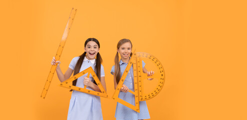 Happy teen girls hold geometric tools for geometry lesson orange background copy space, school