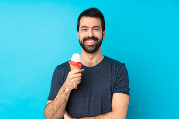 Young man with a cornet ice cream over isolated blue background keeping the arms crossed in frontal...