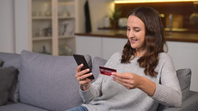 Headshot of excited young woman doing long awaited purchase online, happy female holds smartphone and a credit card, shopping online, making purchase. Consumerism concept