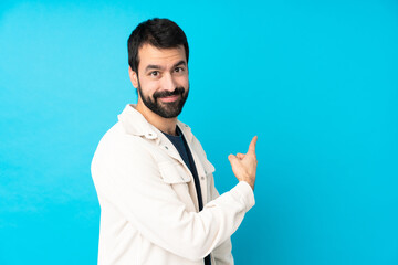 Young handsome man with white corduroy jacket over isolated blue background pointing back