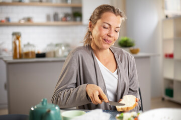  Beautiful woman enjoying in breakfast. Happy young woman eating sandwich at home.