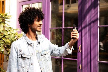 Young man enjoying outdoors. Handsome man with curly hair using the phone, having video call.