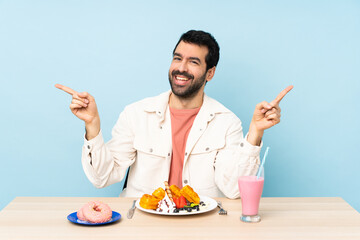 Man at a table having breakfast waffles and a milkshake pointing finger to the laterals and happy