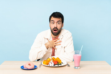 Man at a table having breakfast waffles and a milkshake surprised and shocked while looking right