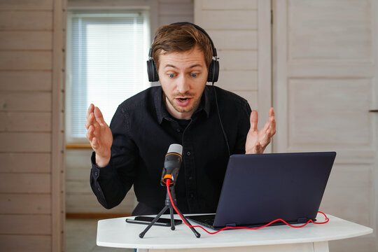 Young Hipster Man With Headphones Recording Podcast Using Laptop At Home Studio, Broadcasting An Interview Using Microphone.