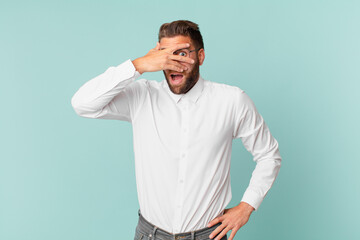 young handsome man looking shocked, scared or terrified, covering face with hand