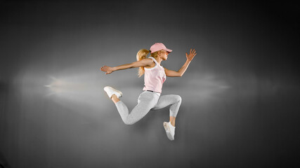 Fototapeta na wymiar Young woman with fit body jumping and running against grey backg