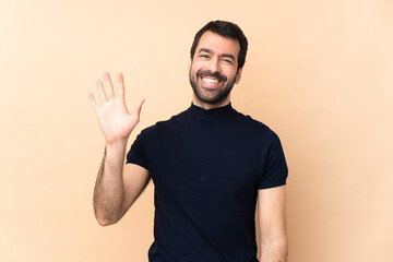 Caucasian handsome man over isolated background saluting with hand with happy expression