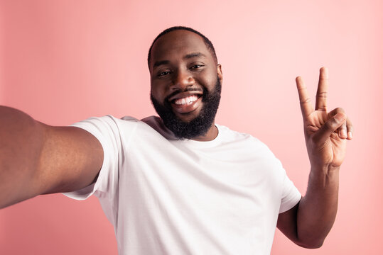 Portrait of cheerful positive man take selfie show v-sign beaming smile on pink wall