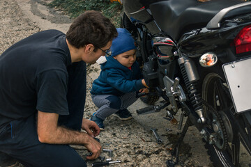 Father-son communication. A father on the street shows his young son how to fix a motorcycle.