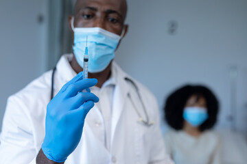 African american male doctor in face mask and gloves preparing covid vaccination for sick patient