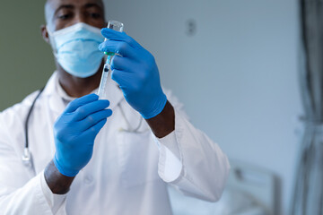 African american male doctor wearing face mask and gloves preparing covid vaccination