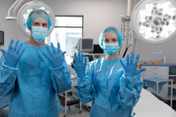 Portrait of caucasian male and female surgeons standing in operating theatre wearing face mask