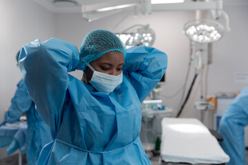 Fototapeta na wymiar Portrait of mixed race female surgeon in operating theatre putting on face mask