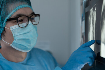 Mixed race male surgeon in operating theatre wearing face mask looking at screen