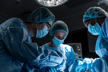 Diverse group of male and female surgeons in operating theatre wearing face masks performing surgery - Powered by Adobe