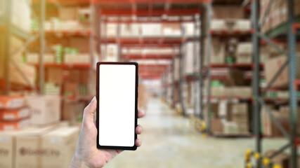 Woman hand holding smart phone with blank screen in blur warehouse background, close up, copy space