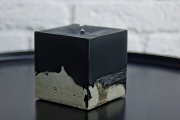 homemade black candle with concrete on the background of a white wall. handmade decor close-up. Details of colored candle in loft style in the shape of a cube