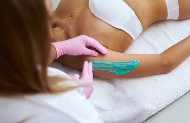 A master beautician carries out epilation on his hands with a blue paste