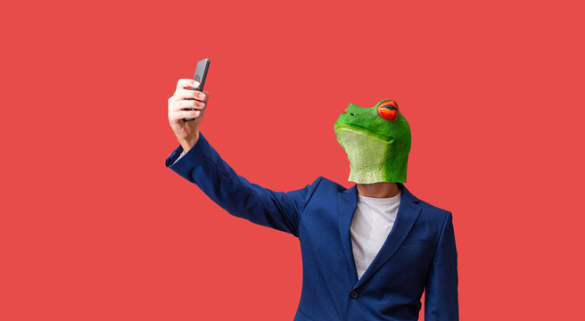 Man With Googly-eyed Frog Mask Taking A Selfie With Smart Phone On Red Background