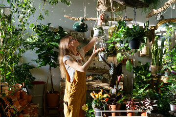 Busy gardener, small business owner florist female in plant store work with potted houseplants over...