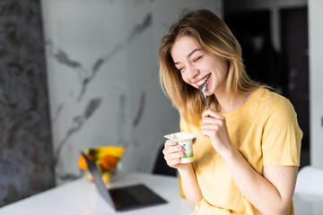 Shot of confident young woman working with computer while with computer while eating yogurt sitting...