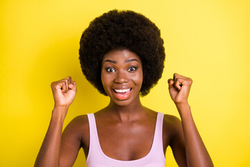 Photo of surprised young dark skin woman winner excited raise fists celebrate isolated on yellow color background