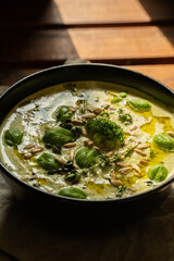Broccoli cream soup decorating with seeds, basil, olive oil in a black bowl on a wooden table