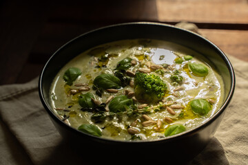 Broccoli cream soup decorating with seeds, basil, olive oil in a black bowl on a wooden table