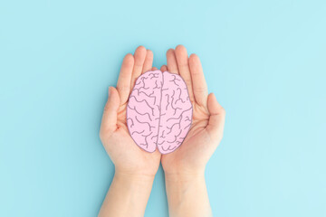 Woman hands holding human brain shape made from paper on light blue background. Awareness of Alzheimer, Parkinson's disease, dementia, stroke, seizure or mental health. Neurology and Psychology care.