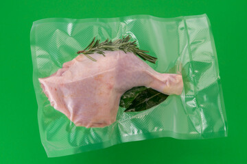 Chicken thighs in vacuum packed sealed for sous vide cooking with rosemary, bay leaf and sage , isolated on green background