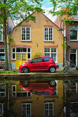Fototapeta na wymiar Red car on canal embankment in street of Delft. Delft, Netherlands