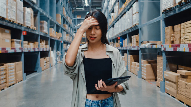 Unhappy young Asia businesswoman looking and feeling confused using digital tablet checking inventory levels standing in retail shopping center. Distribution, Logistics, Packages ready for shipment.