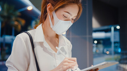 Young Asia businesswoman in fashion office clothes wear medical face mask using smart pen for write...