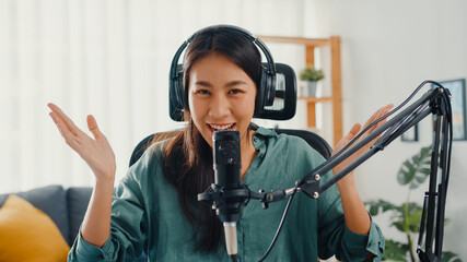 Happy asia girl record a podcast with headphones and microphone look at camera  talk and take a rest in her room. Female podcaster make audio podcast from her home studio, Stay at house concept. - obrazy, fototapety, plakaty