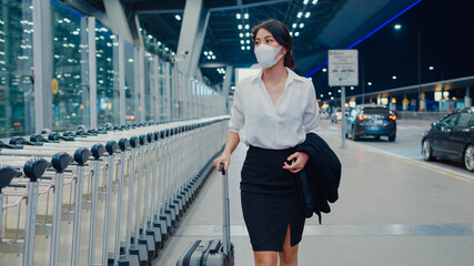 Asian business girl arrive destination wear face mask with drag luggage walk outside wait car...