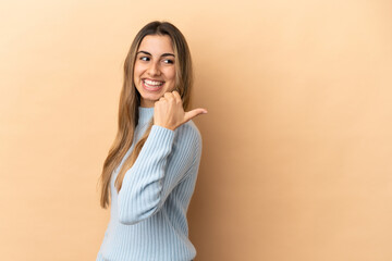 Young caucasian woman isolated on beige background pointing to the side to present a product