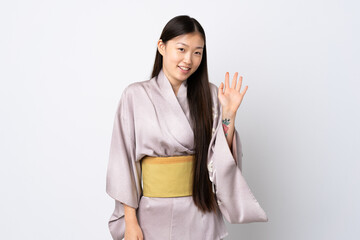 Young Chinese girl wearing kimono over isolated background saluting with hand with happy expression