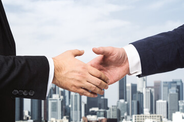 Two businessmen shake hands on the background of sunny city skyline, deal concept, close up